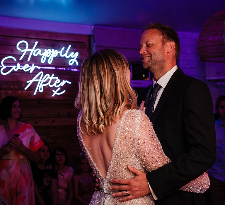 The bride and groom share their first dance together with neon wedding sign 