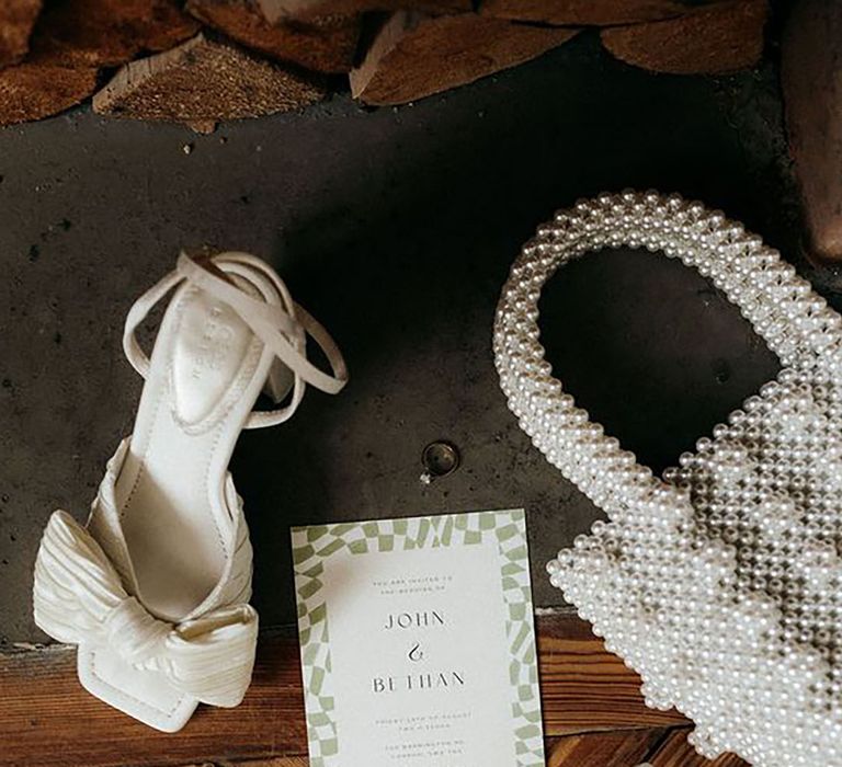 Image of pearl bridal bag, heeled shoes and a wedding invitation by Caitlin & Jones Photography