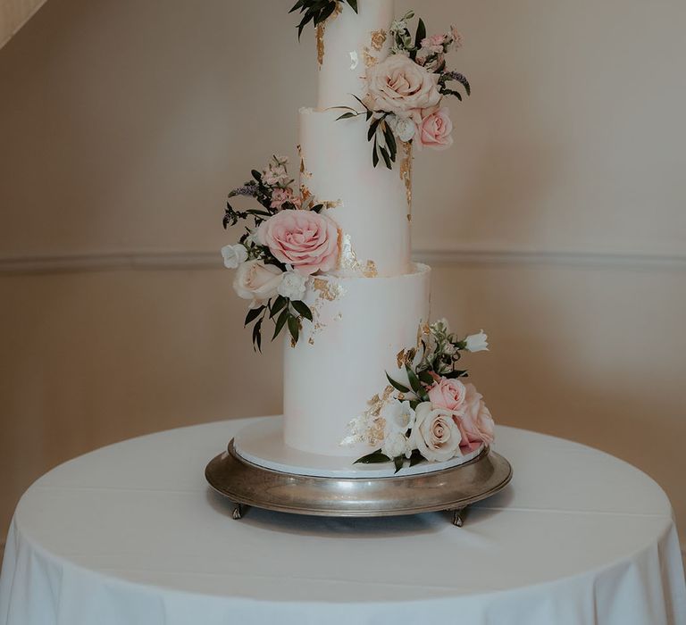 Traditional and classic white iced three tier wedding cake with pink flowers and gold flakes 