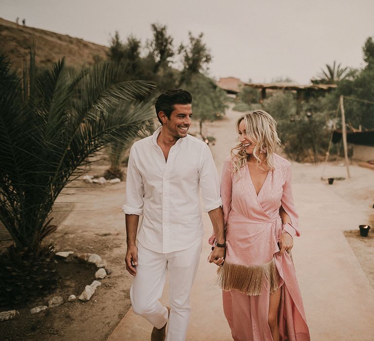 Groom all in white and bride in a pink dress with gold tassels 