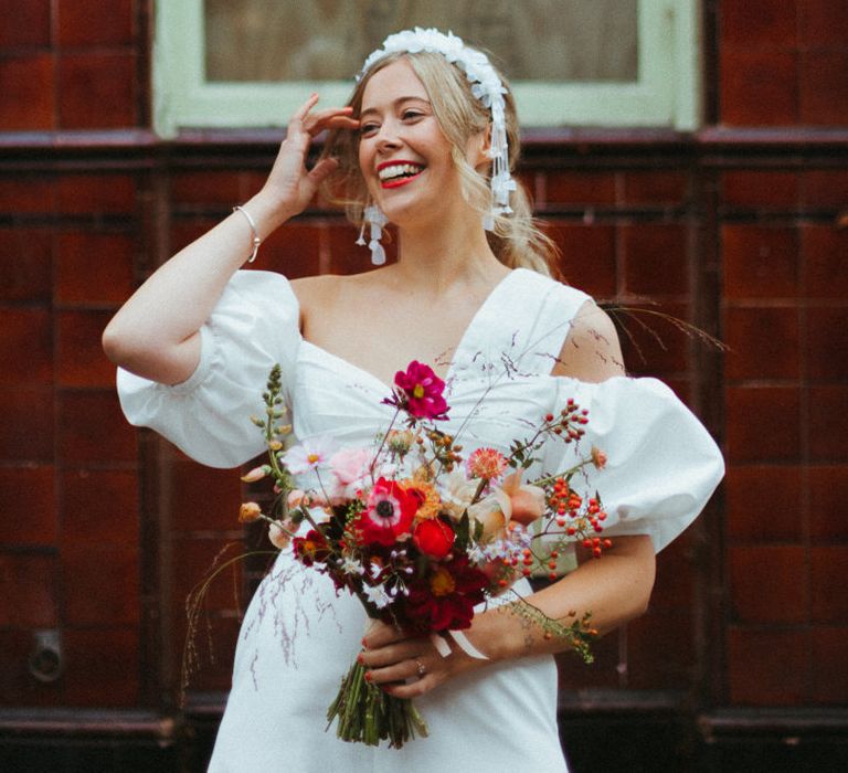 Smiling bride poses solo for micro wedding in London with puff sleeve dress and a ruffle headband