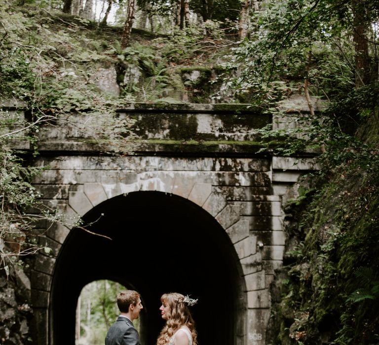 Bride and groom stand under a bridge together in their family tartan pattern