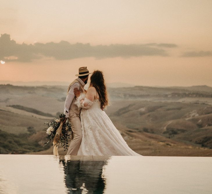 Groom holding olive bouquet as they look over Tuscany countryside