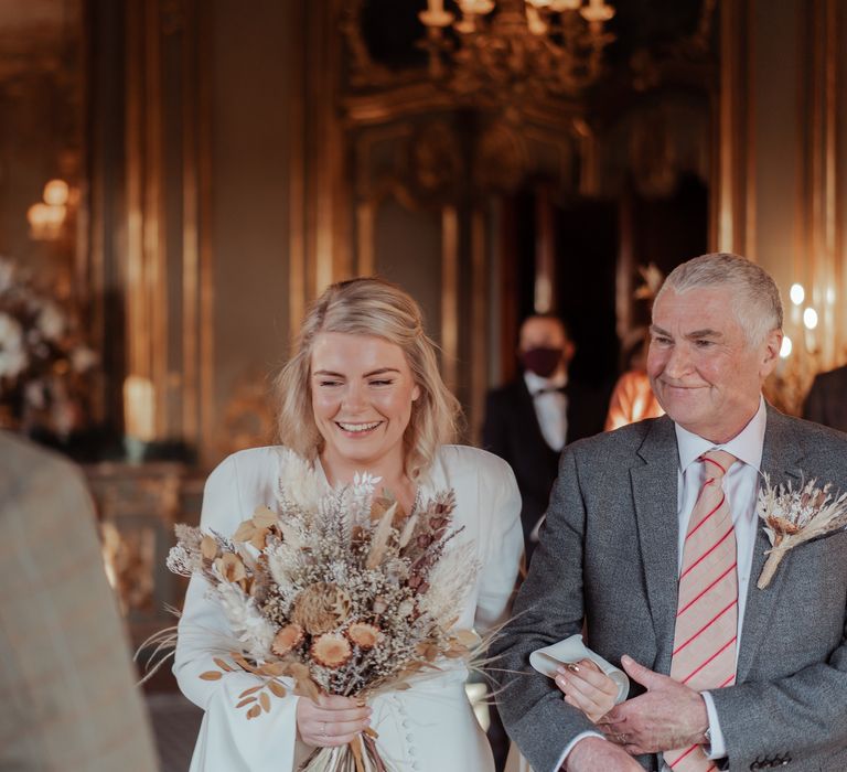 Bride walks in wearing Ghost wedding dress carrying dried floral bouquet 