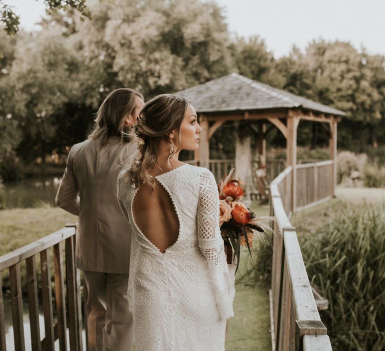 Bride & groom walk together with bride wearing open back dress with scalloped edge