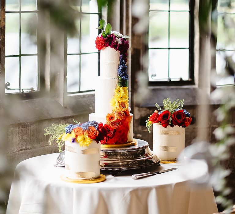 Cake table with tall buttercream wedding cake with brightly coloured floral design down the front and two individual cakes 