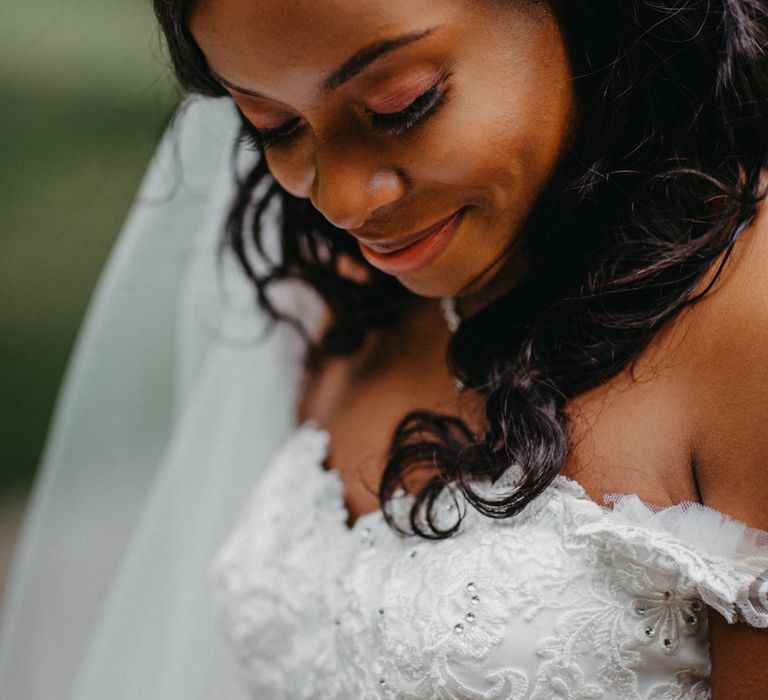 A Black bride looks down smiling in an off the shoulder dress