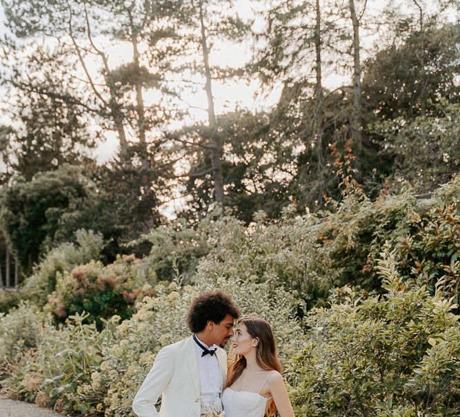 Black groom in a white tuxedo jacket looking into his brides eyes 