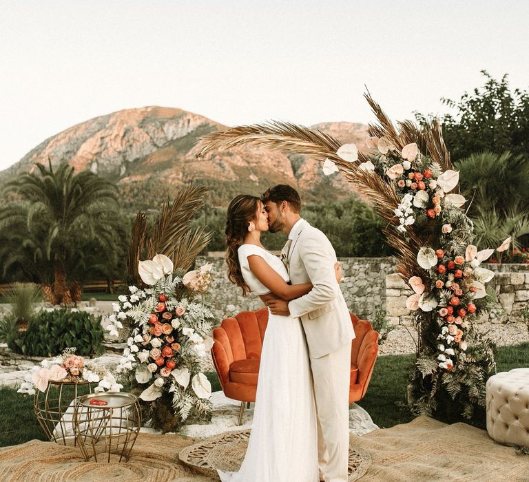 Altar with wicker rugs, velvet love seat and boho wedding flowers including anthuriums, roses and foliage