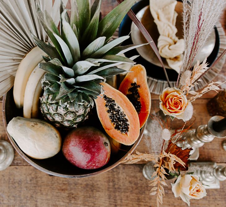 Fruit bowl complete surrounded by candles and dried flowers atop a wooden table