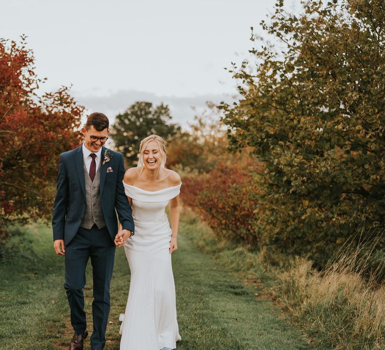 Bride & groom walk together through countryside surrounded by greenery