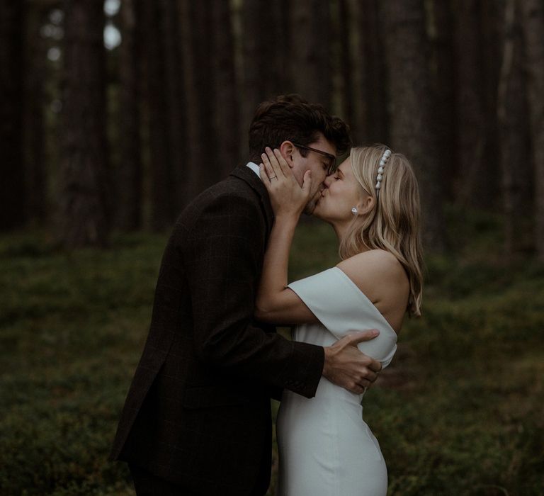 Bride & groom kiss underneath trees whilst in the woodlands