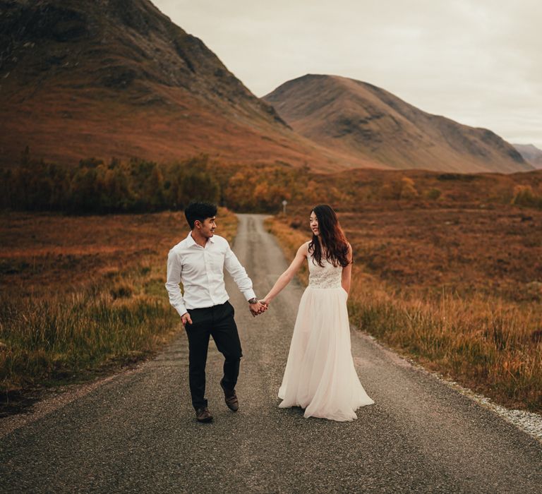 Couple walk down an empty road in Scotland surrounded by mountains