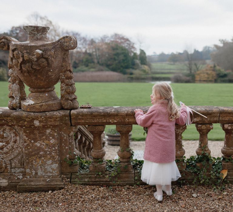 Child at Brympton House wedding wearing pink coat, tulle white skirt and silver ballerina shoes