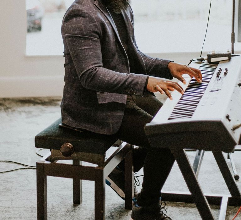 Man in grey checked blazer and black top sits playing keyboard at Bridge Community Church wedding