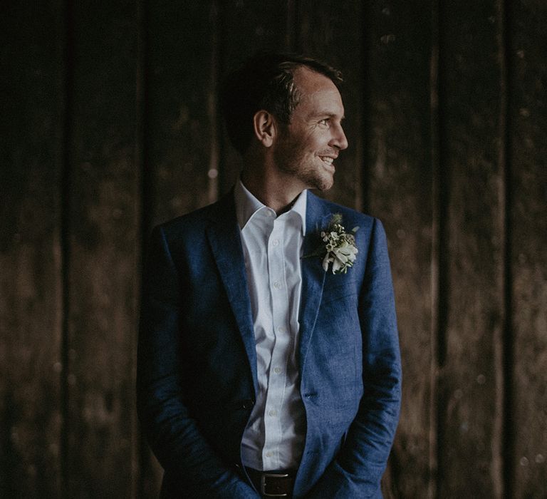 Groom stands with hands crossed and looks to the side smiling on wedding day