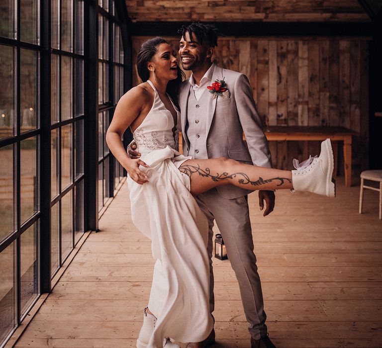 Bride lifts leg wearing white wedding Dr Martens as groom stands beside her 