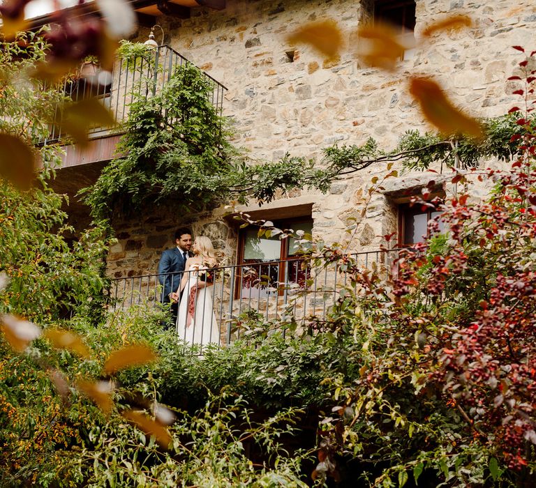 The bride and groom standing on a balcony surrounded by flowers and foliage at Podere Conti