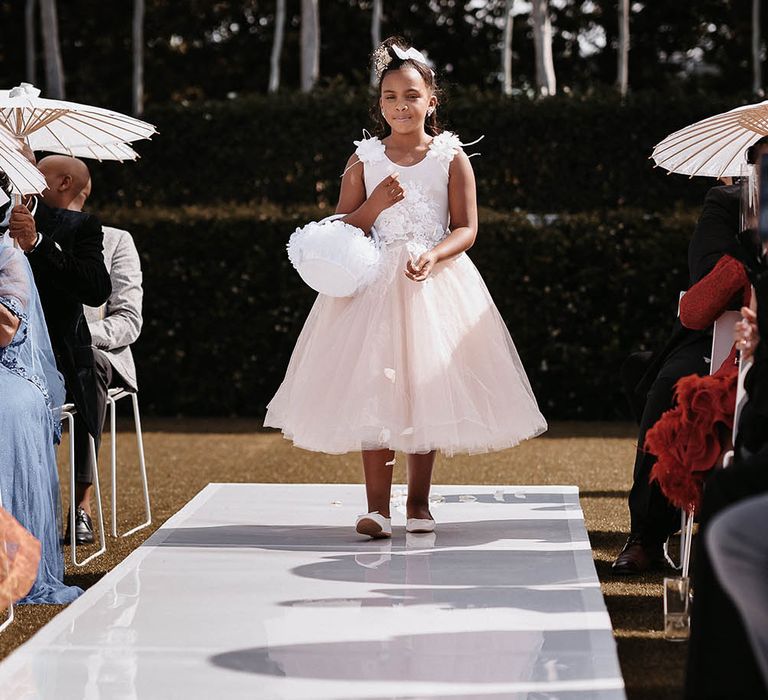 Young bridesmaid in a pink and white tulle and lace dress waling down the aisle with a petal basket 