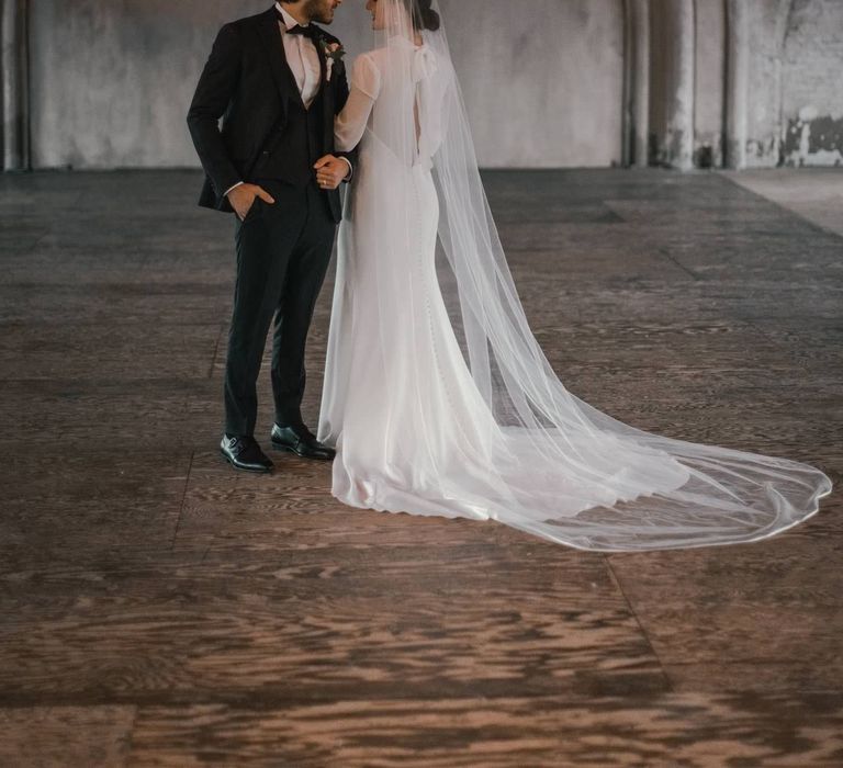 Bride & groom stand in grey space whilst they look at one another