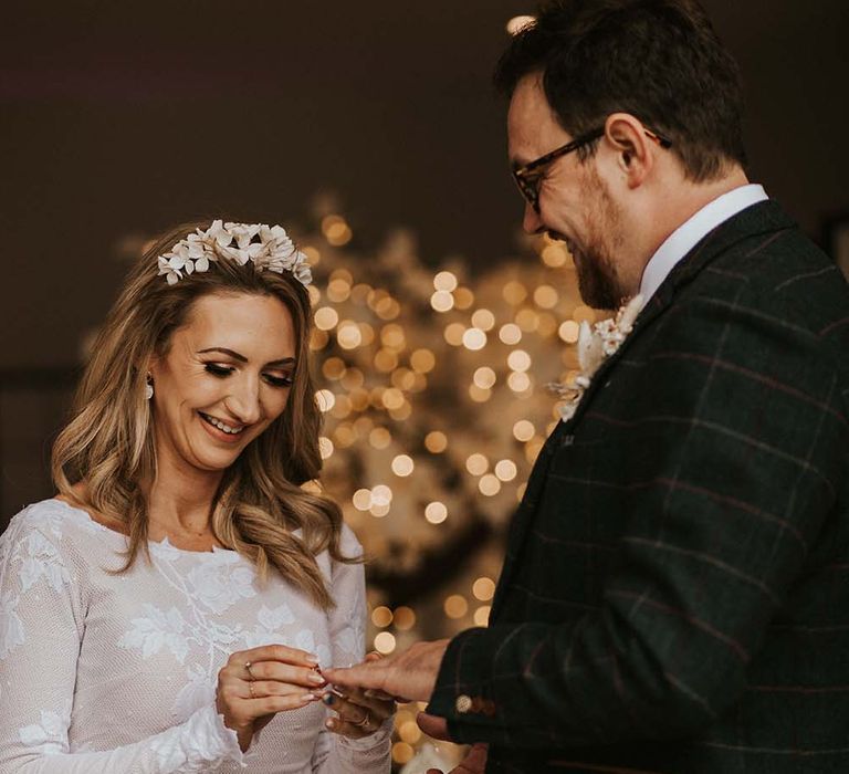 Bride in a fitted wedding dress with appliqué design putting on her grooms wedding ring 