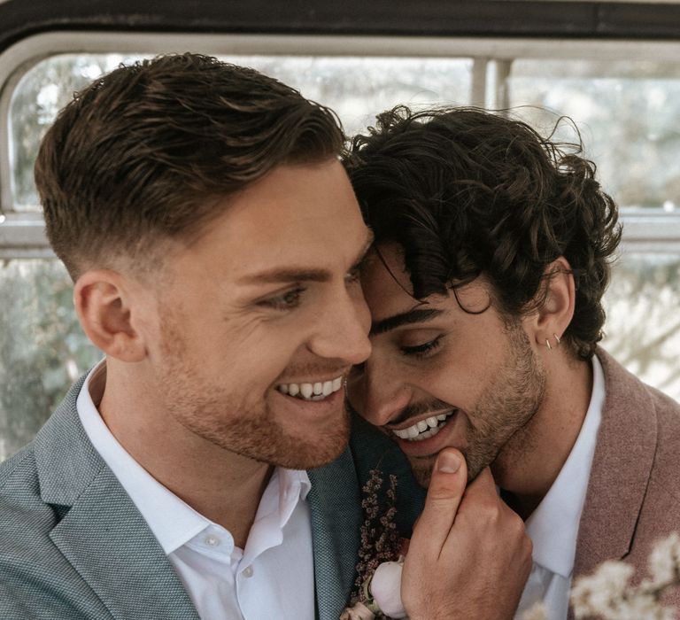 Grooms laugh outdoors during wedding day whilst wearing pastel suits