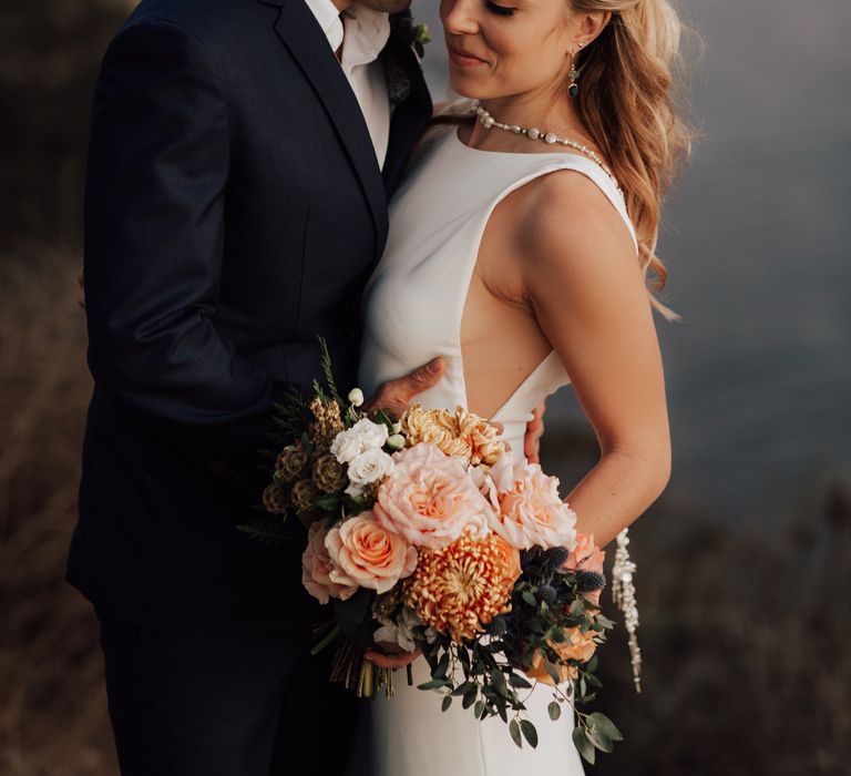 Groom kisses bride on the cheek as she carries peach bouquet on her wedding day