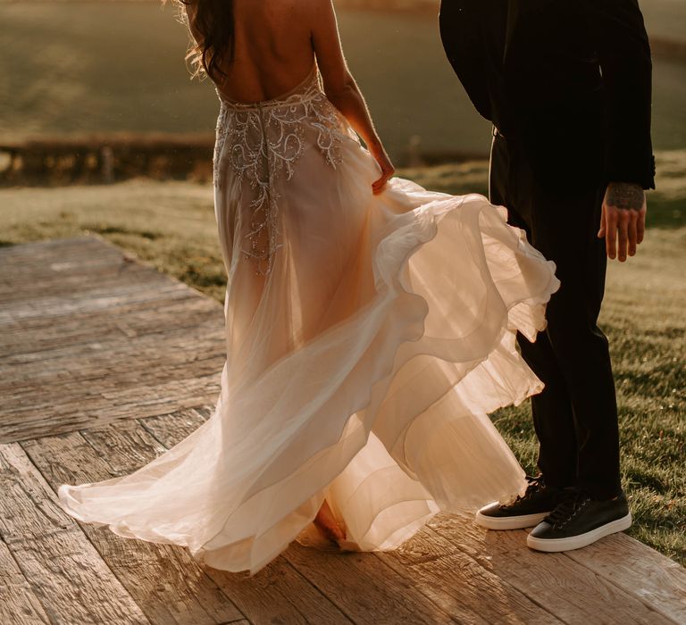 Groom in a black suit and shirt twilling his bride in a low back lace and chiffon wedding dress during golden hour 