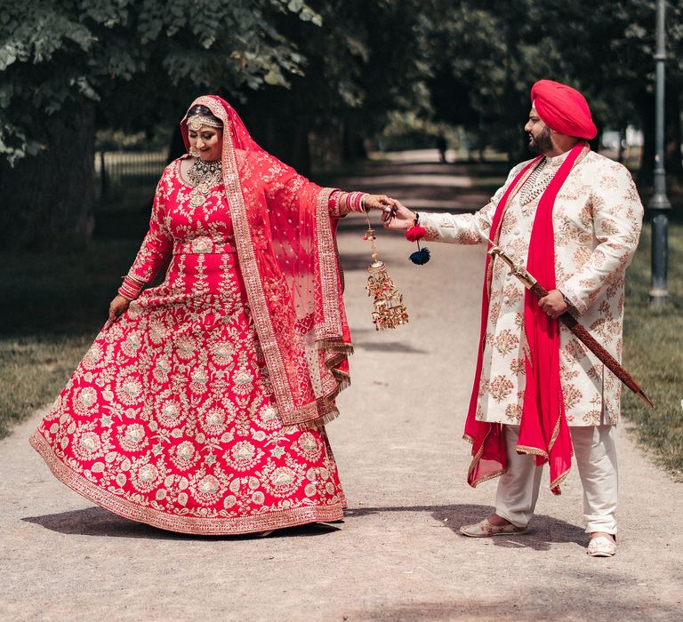 Sikh bride & groom stand outside with one another wearing traditional clothing in bright reds and creams