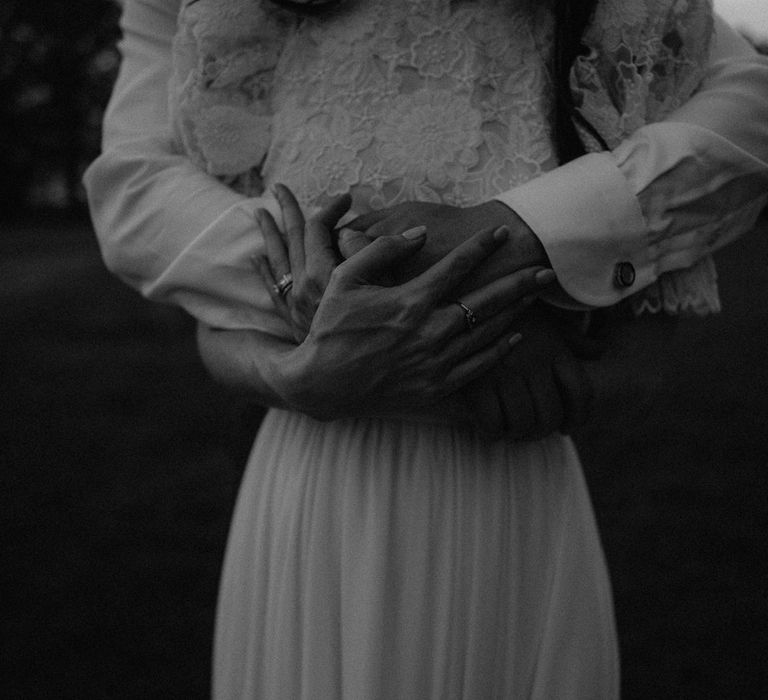 Close up of bride and grooms hands with wedding bands as they stand hugging in the grounds of Loseley Park in Surrey