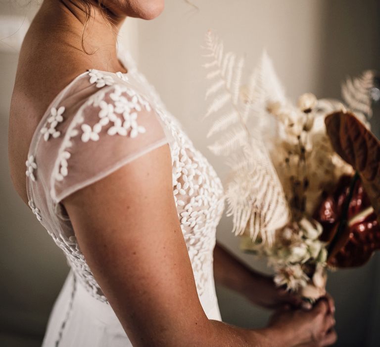 Smiling bride with wedding guppy in open back Rime Arodaky wedding dress with button detailing holds dried bridal bouquet before summer wedding in Dorset