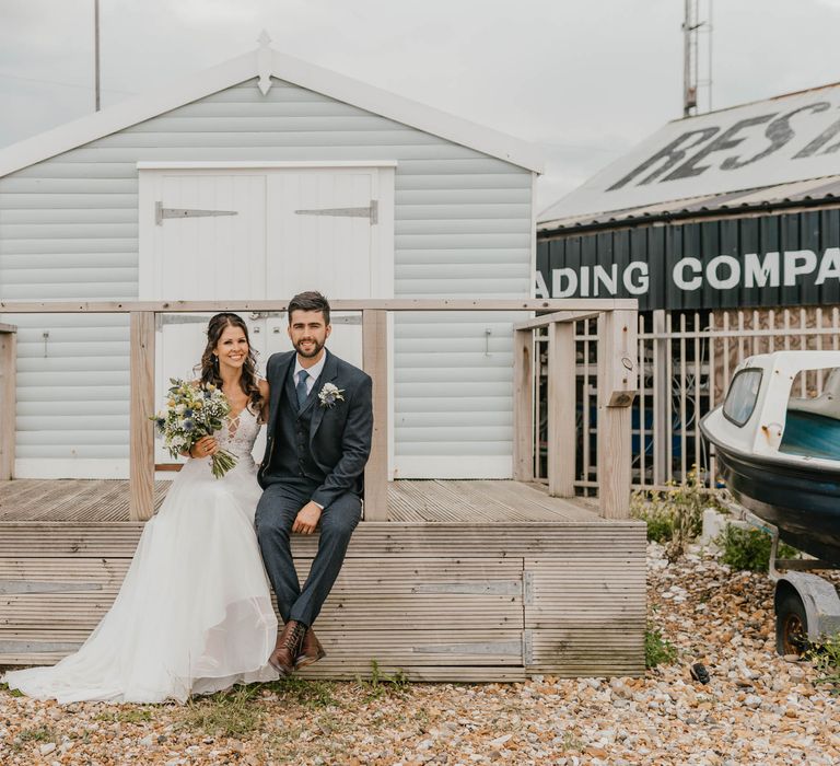 Bride & groom stand in front of beach hut