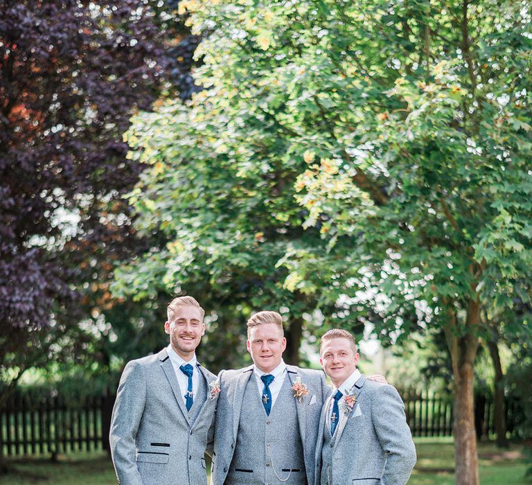 Groomsmen in light grey wool wedding suits with a blue tie and pink buttonhole flower 