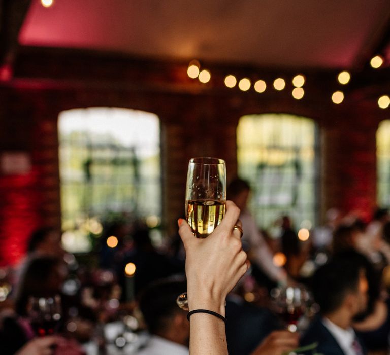 Wedding guest holding up glass of sparkling wine during wedding breakfast at Loft Studios London