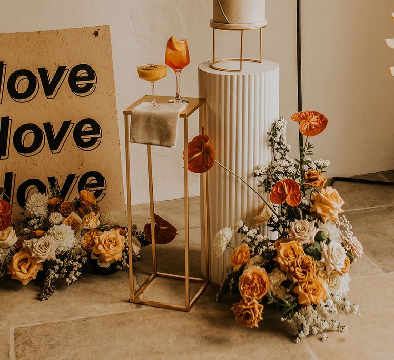 Contemporary marble wedding cake, wedding signs and cocktails surrounded by orange and yellow wedding flowers 