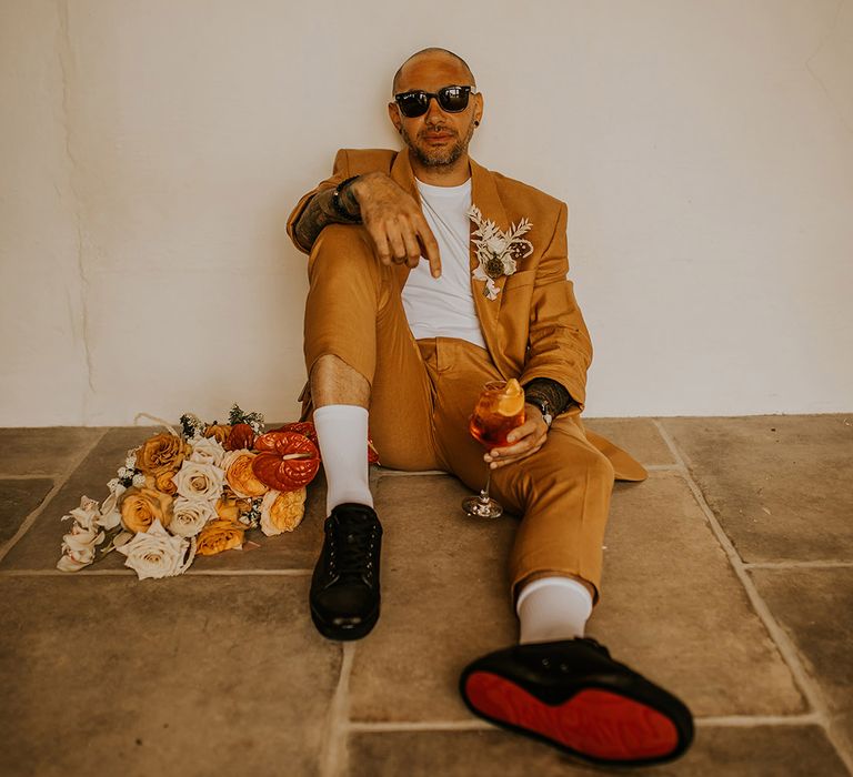 Groom in a mustard orange suit sitting on the floor 