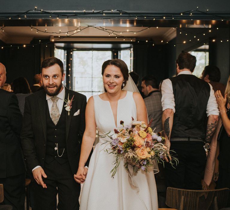 Bride clutches flower bouquet as she walks down the aisle with her new husband