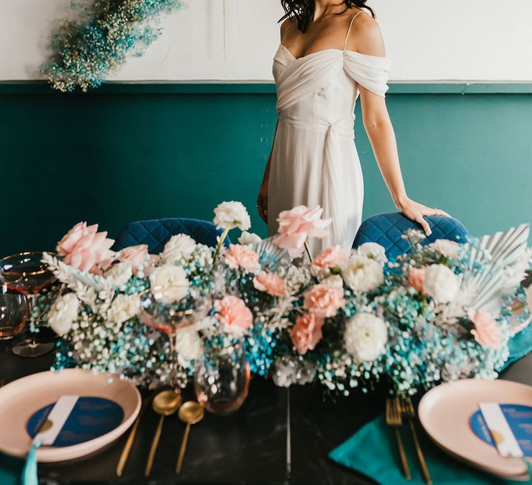 Bride in a cold shoulder wedding dress standing next to her reception table decorated in white and teal gypsophila flowers 