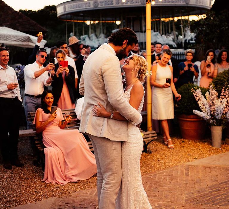 Outdoor first dance with groom in a beige suit and bride in a lace wedding dress