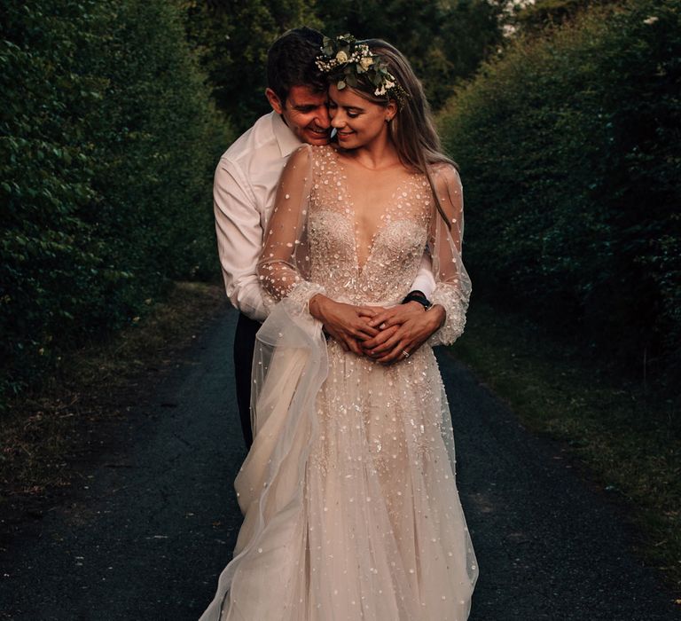 Bride in long sleeve embroidered wedding dress with boho flower crown dances with groom in white shirt and red tie during golden hour