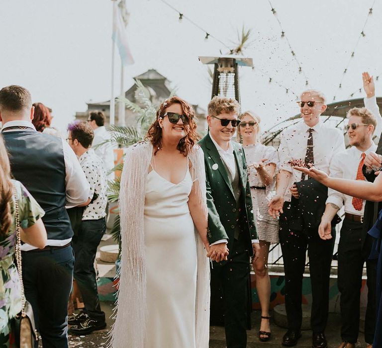 Bride & groom hold hands as they walk through confetti on their wedding day