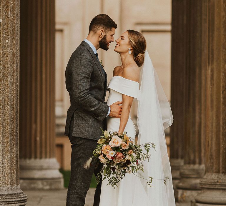 Bride & groom kiss on their wedding day as bride holds floral bouquet