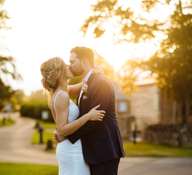 Golden hour portrait with bride and groom kissing at their Summer wedding 