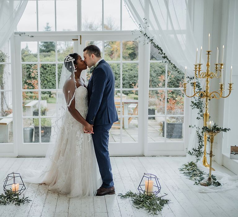 Black bride wears lace veil and wedding dress as she kisses the groom in a classic & rustic pillar candle setting