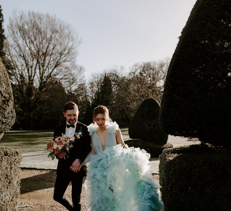 Bride in a dramatic tulle wedding dress with full ruffle skirt and plunging neckline walking through the gardens at Newburgh Priory