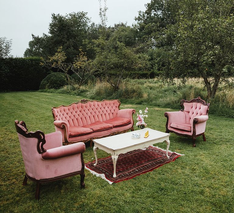 Outdoor seating area for summer wedding with plush pink three-seater sofa and armchairs with white coffee table