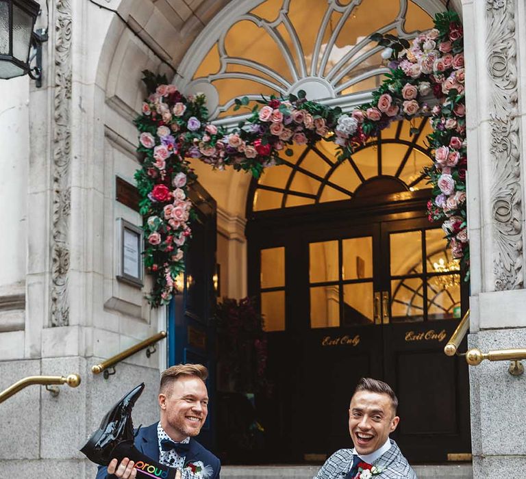 Grooms sit on steps with one another on their wedding day