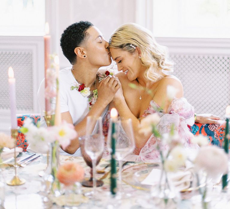 Groom in a white t-shirt and flower collar kissing his bride in a strapless princess wedding dress at their reception table 