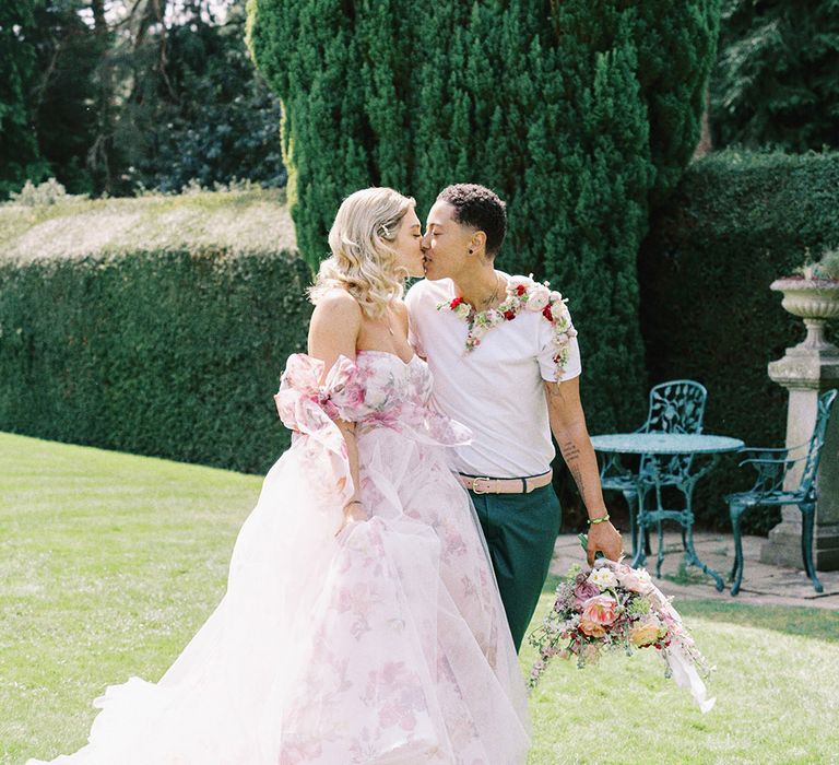 Bride in a strapless pink flower wedding dress kissing her partner in a white t-shirt and flower collar 