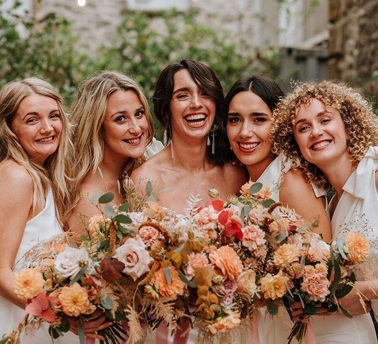 Bride smiles with her stunning bridesmaids in white one shoulder dresses